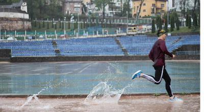 A runner on a race track splashing into a deep puddle